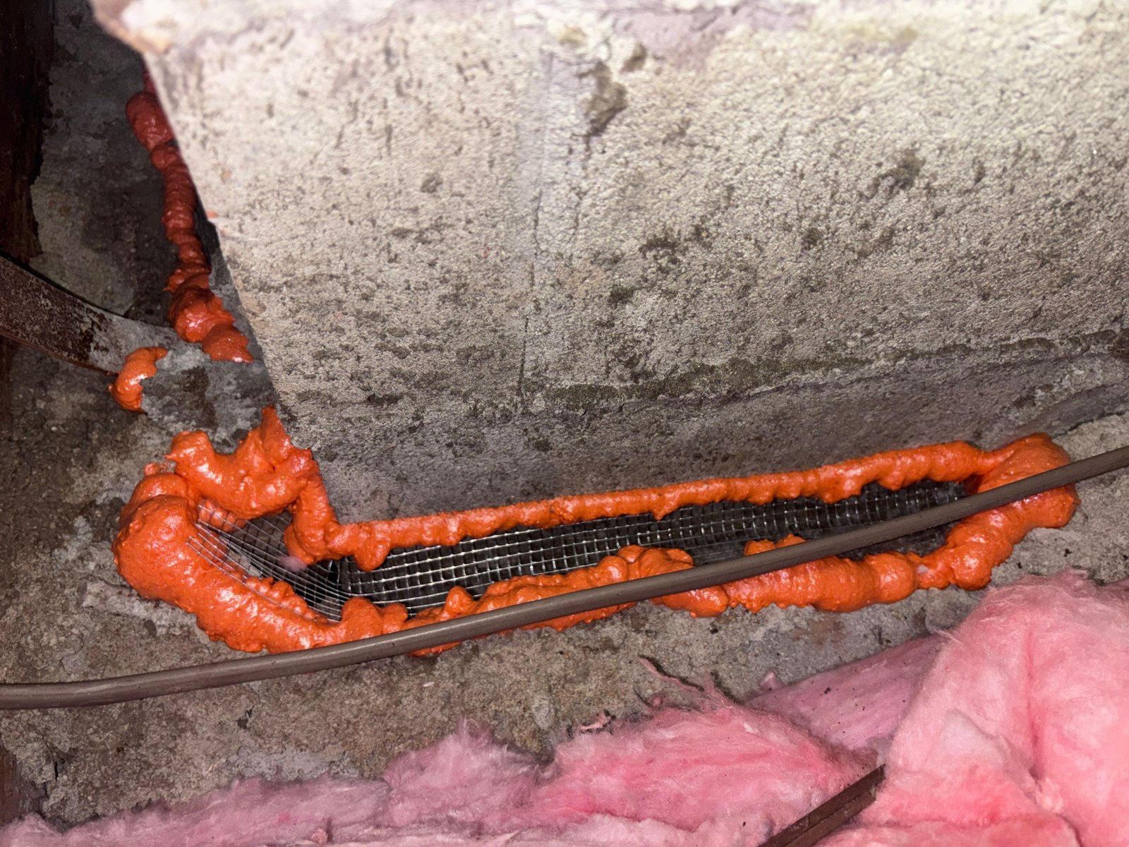 Wire mesh and foam sealing around a chimney base in a Long Beach attic